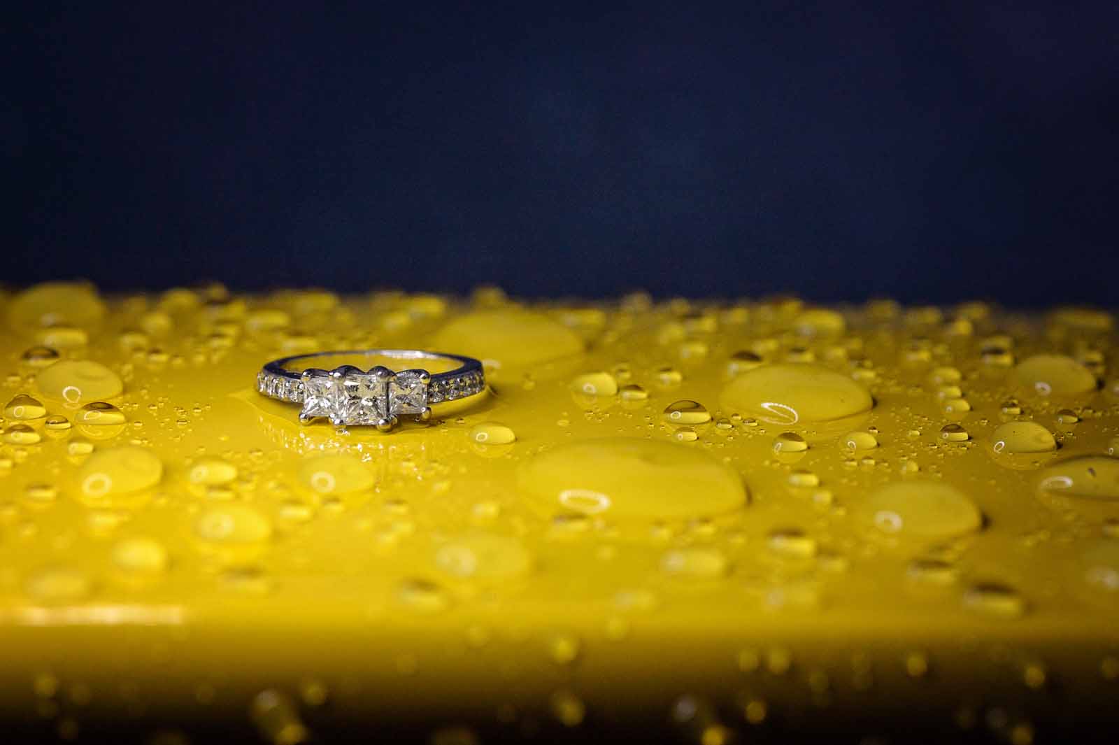An engagement ring sitting on a yellow car with rain drops around in Ottawa