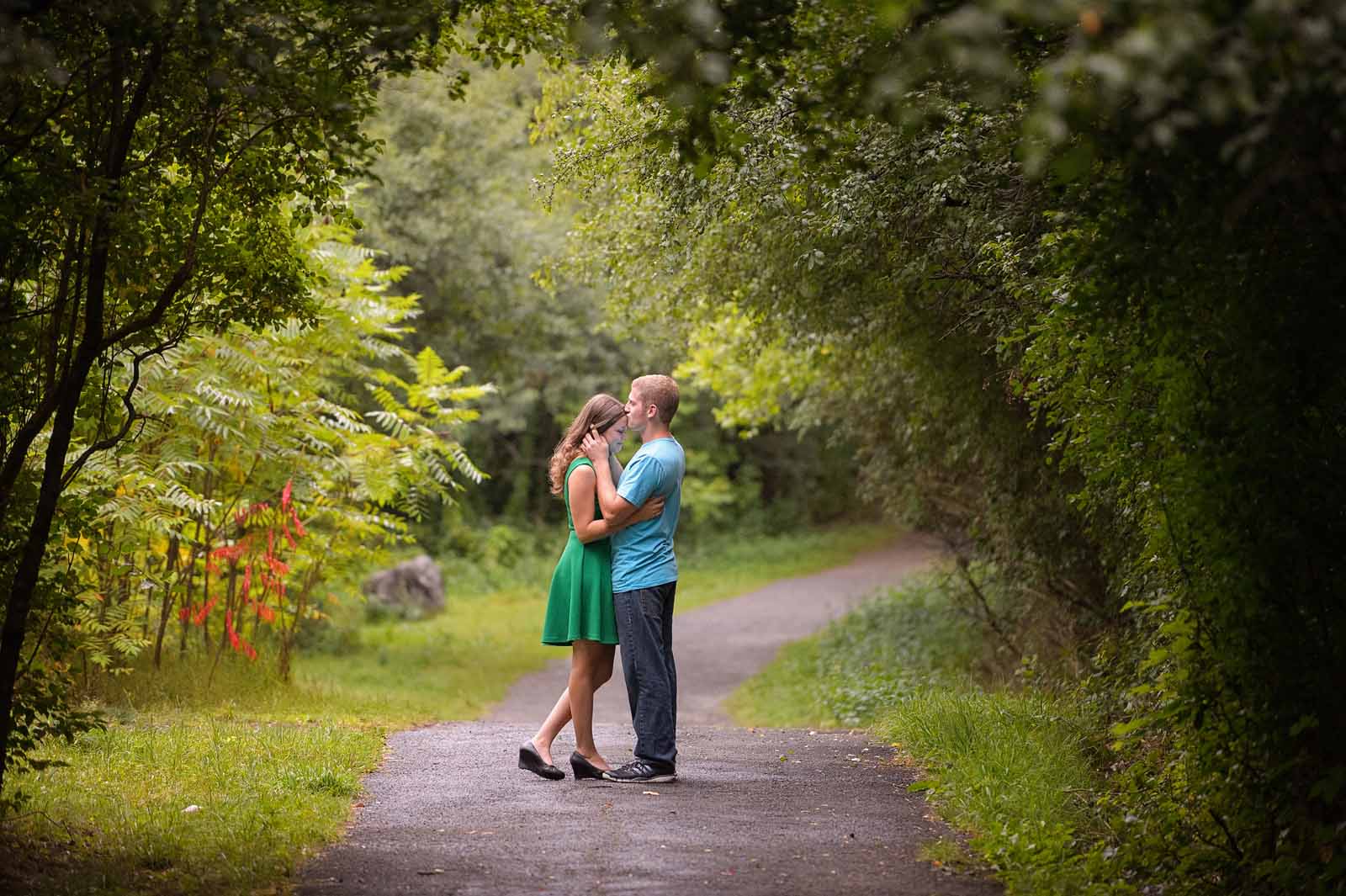 a couple sharing a tender moment and a kiss on a pathway at Hog’s Back Park in Ottawa, Ontario