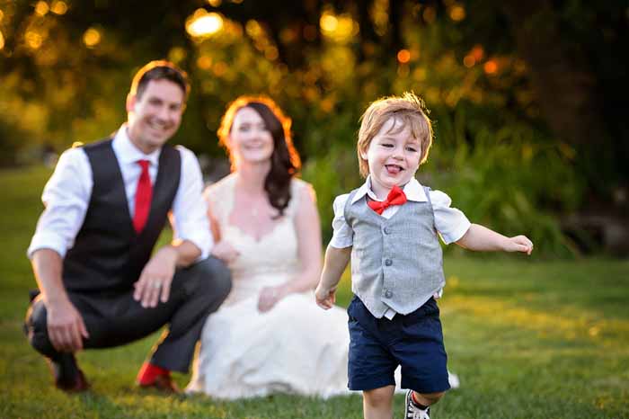 The couple in the background while their son, the ring bearer, runs towards the camera laughing at Stonefields