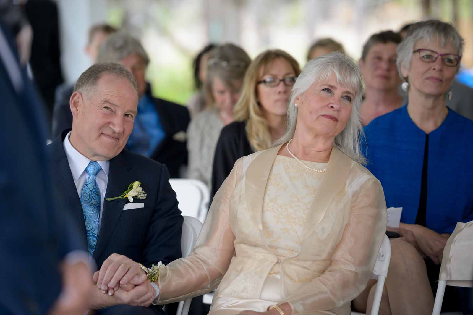 Parents holding hands while they watch their beautiful child get married, under a tent on a hot summer Ottawa afternoon
