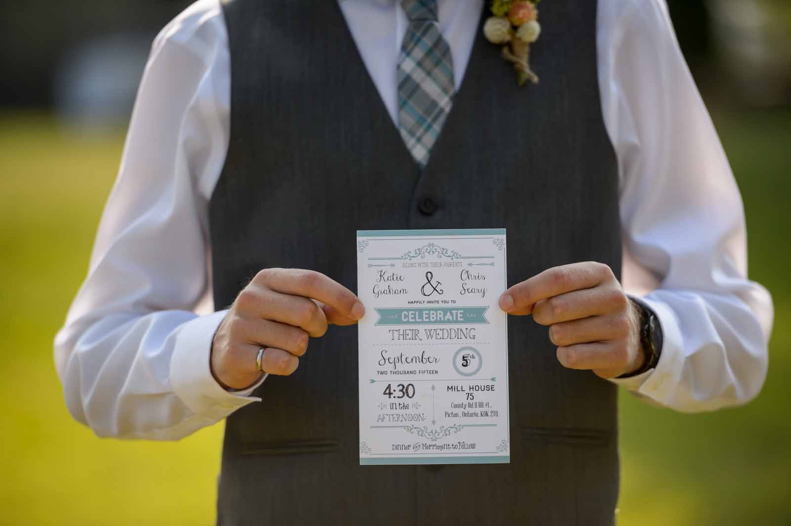 Groomsman holds wedding invitation in his vest with boutenneire