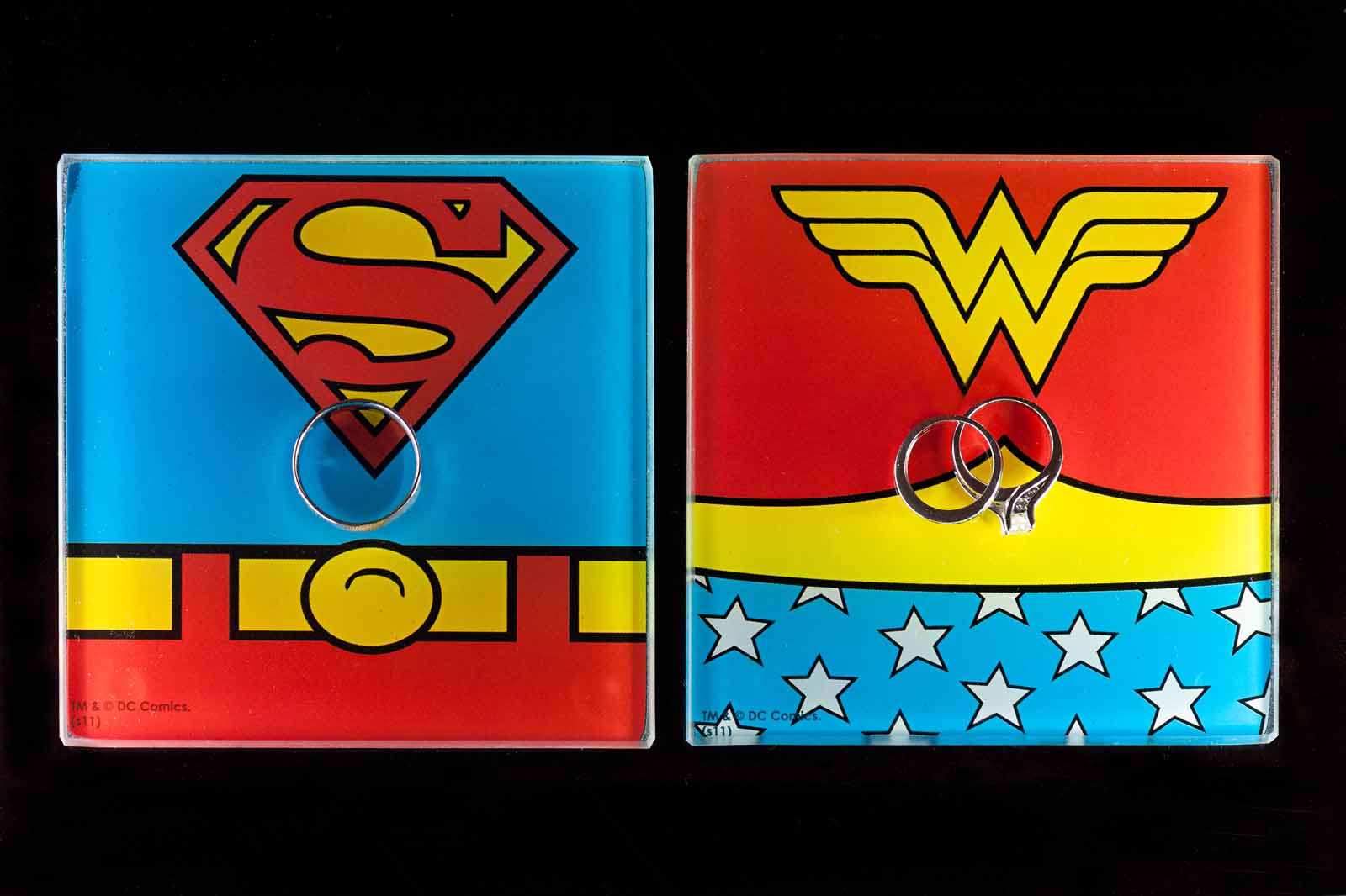 Wedding rings photographed on Superman and Wonder Woman coasters