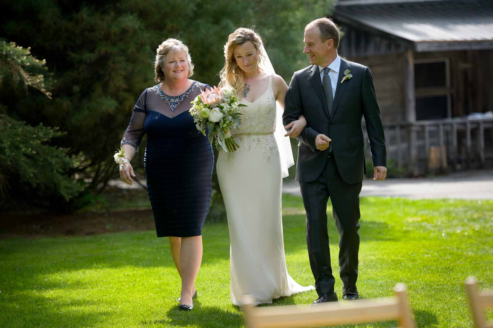 Bride walking down the aisle at her warm May wedding ceremony with her mother and father
