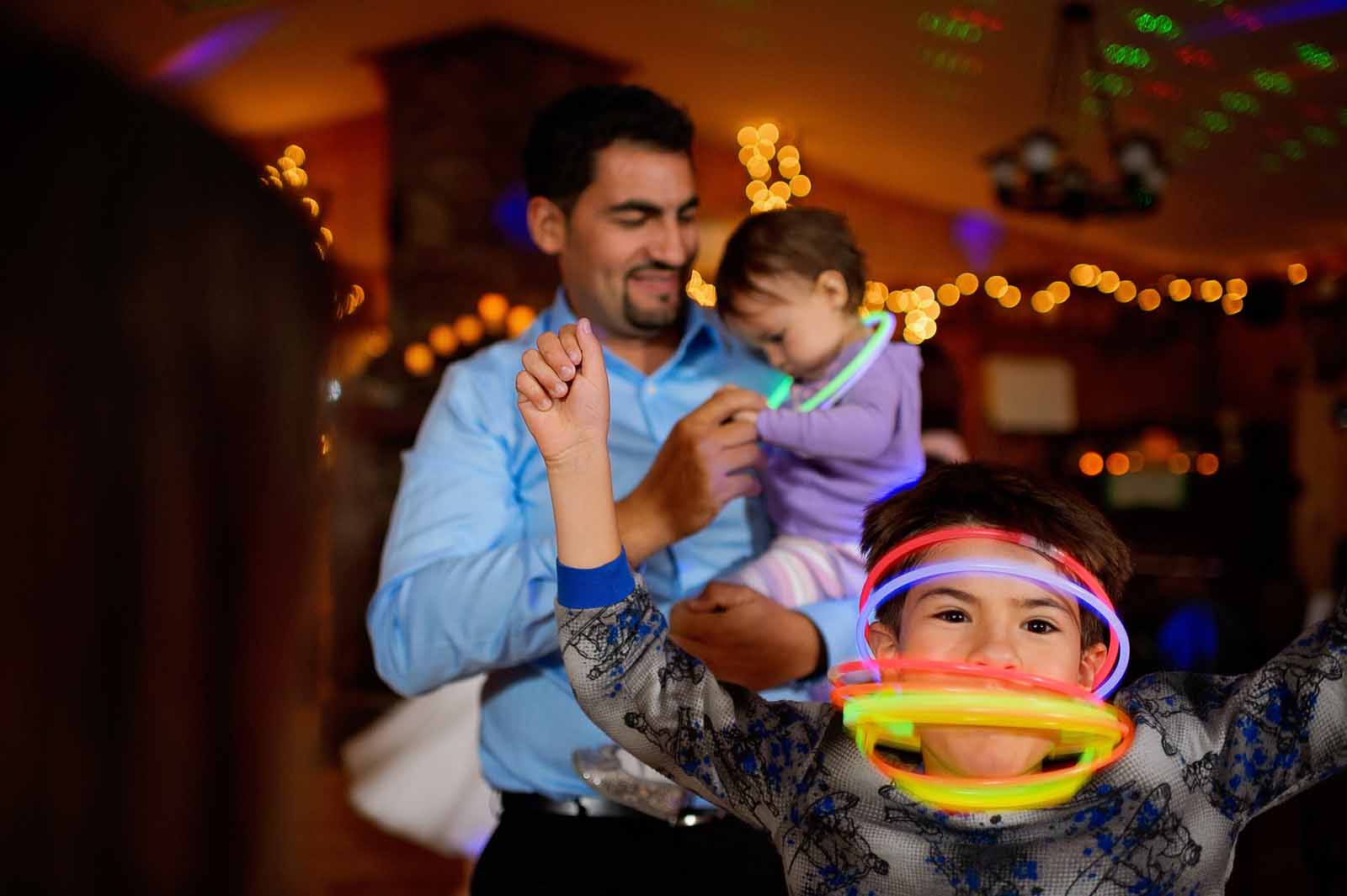 Family dancing at a wedding ceremony with a kid with many glow stick necklaces on