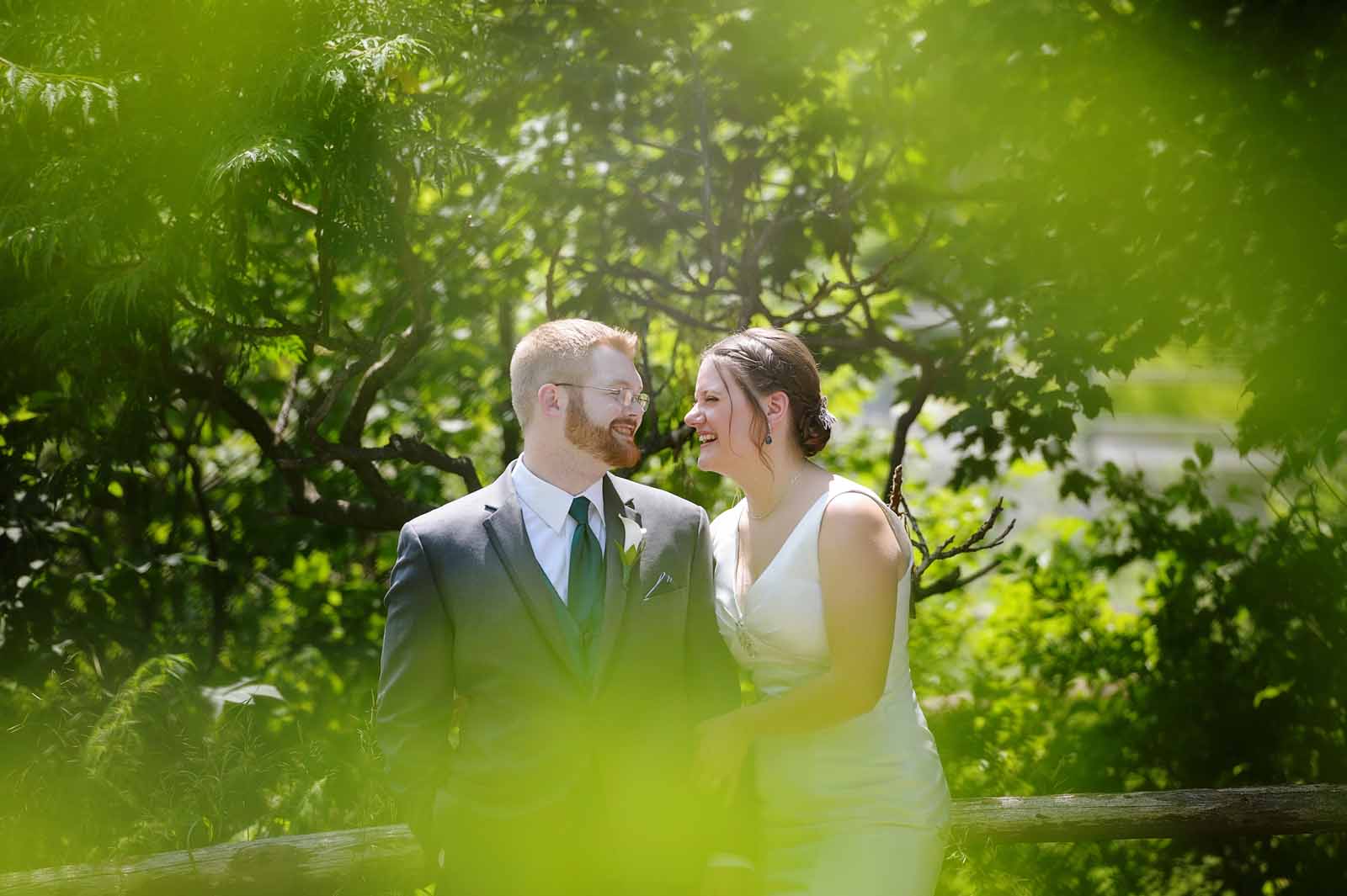 Through the trees, the bride and groom are laughing with each other on their wedding day
