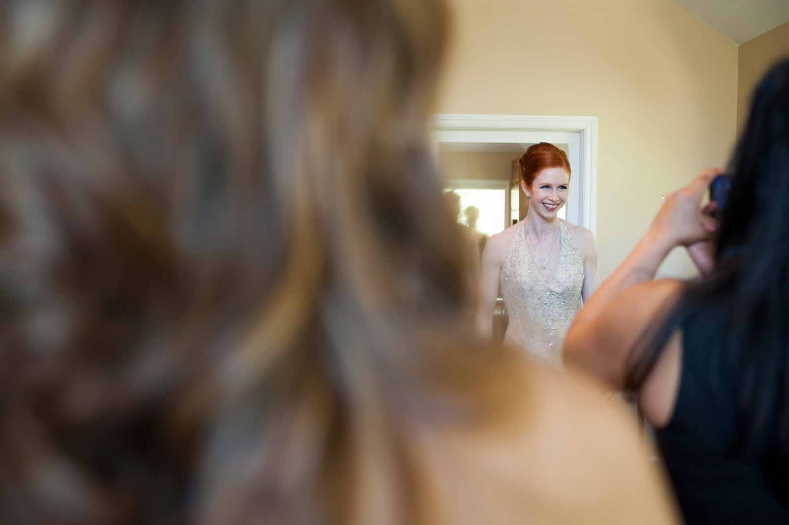 Bride getting ready and her bridesmaids taking pictures of her in her wedding dress