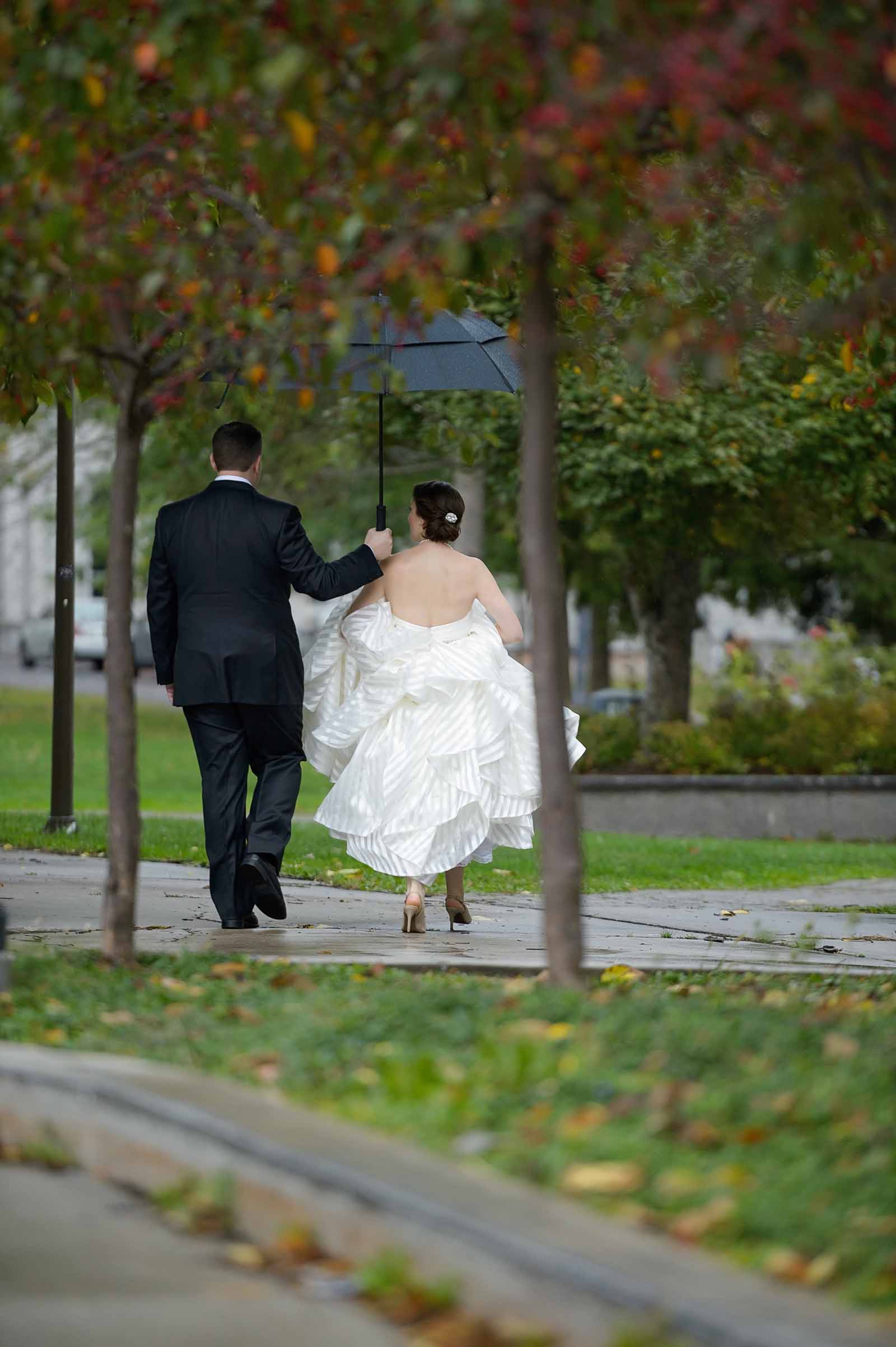 Bride and groom walking in the rain holding an umbrella to keep them dry on their wedding day