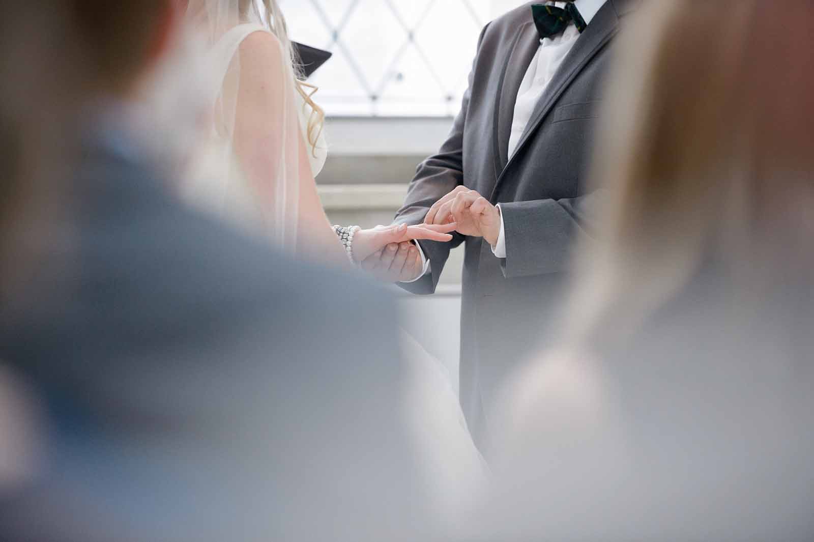 A peek through of the groom putting the ring on the bride finger during their wedding ceremony